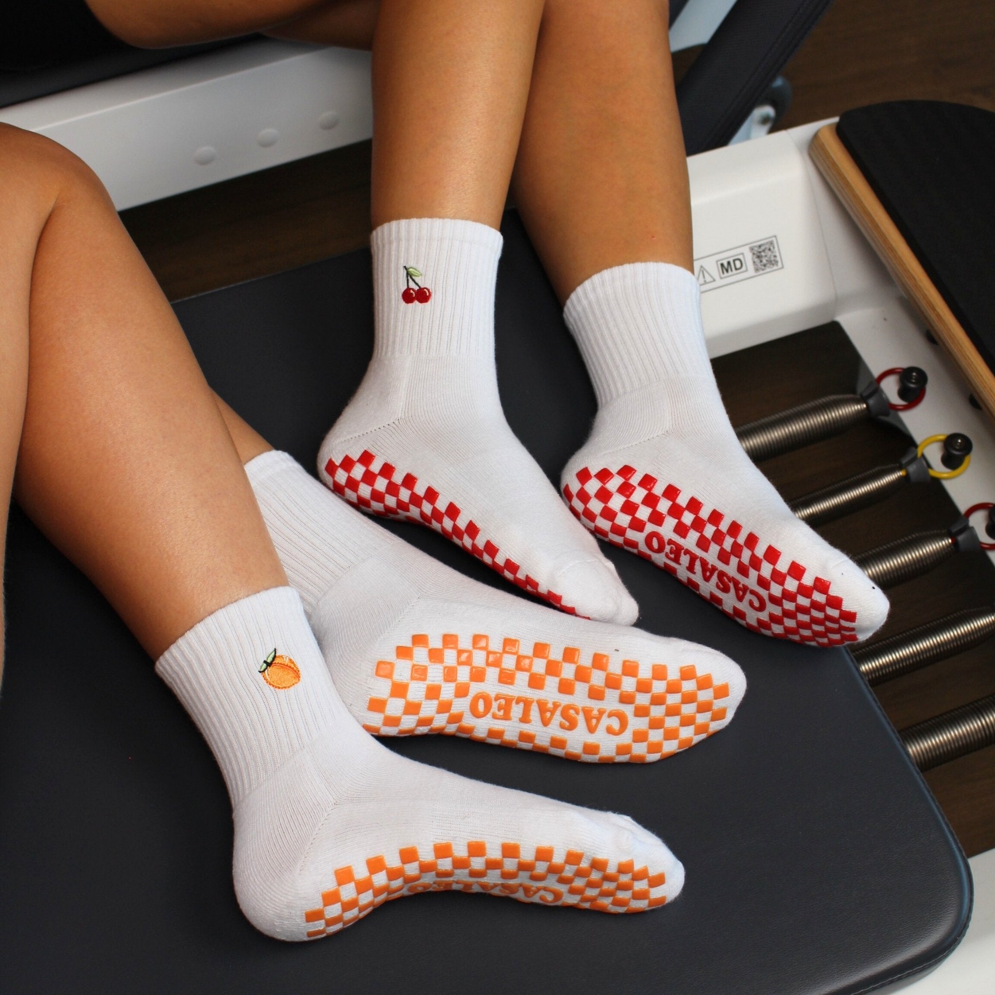 CASALEO Grip Socken mit roter Grip Sohle und Kirsch Icon und orangener Grip Sohle und Pfirsich Icon auf dem Reformer Gerät