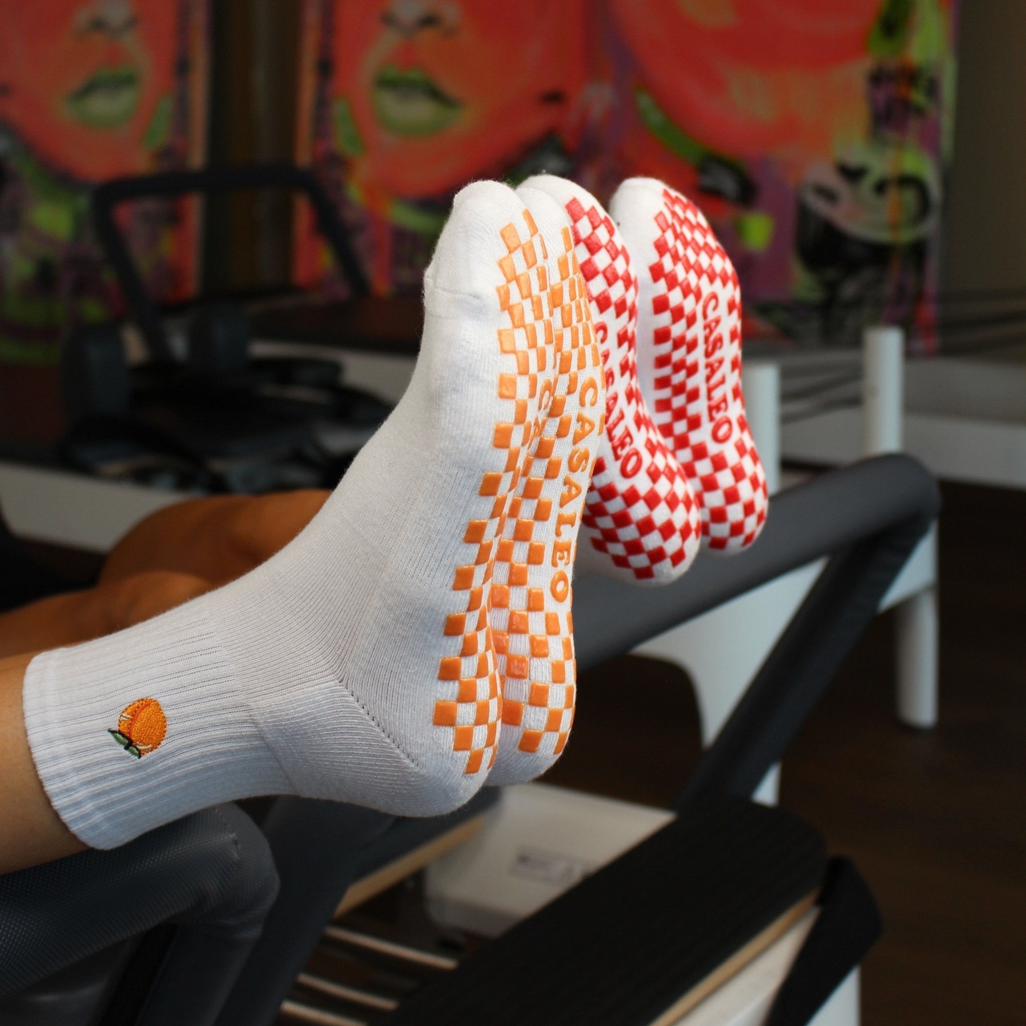 CASALEO Grip Socken mit roter Grip Sohle und Kirsch Icon und orangener Grip Sohle und Pfirsich Icon auf dem Reformer Gerät