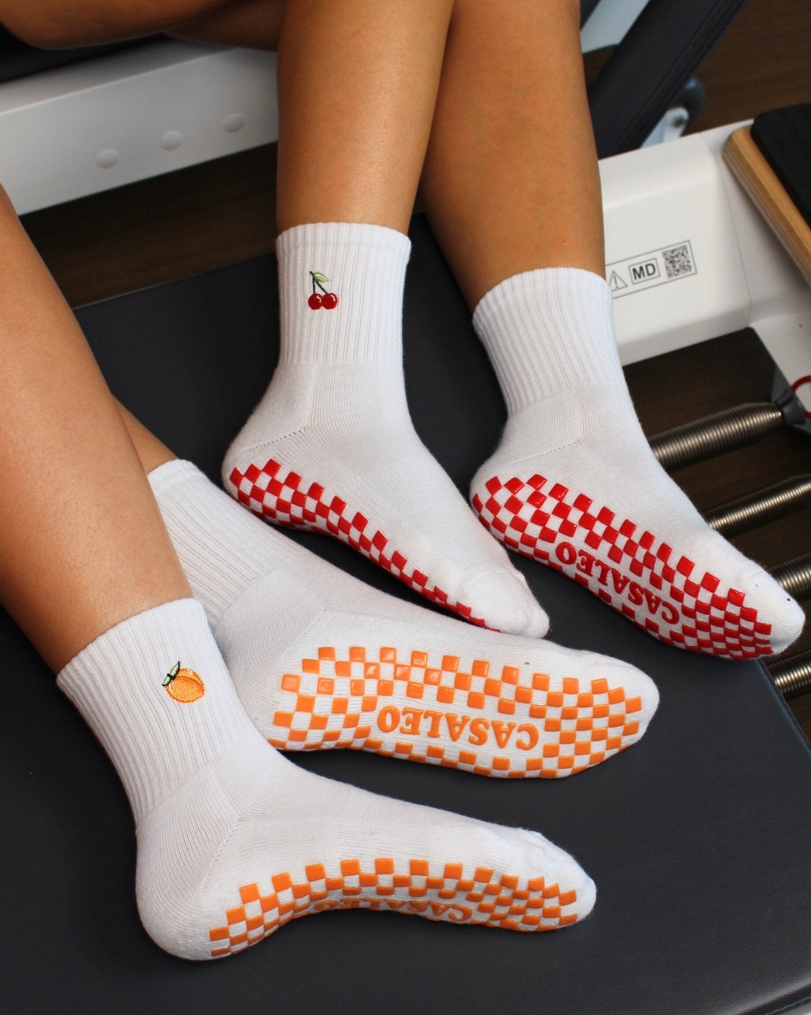 CASALEO Grip Socken mit roter Grip Sohle und Kirsch Icon und orangener Grip Sohle und Pfirsich Icon auf dem Reformer Gerät