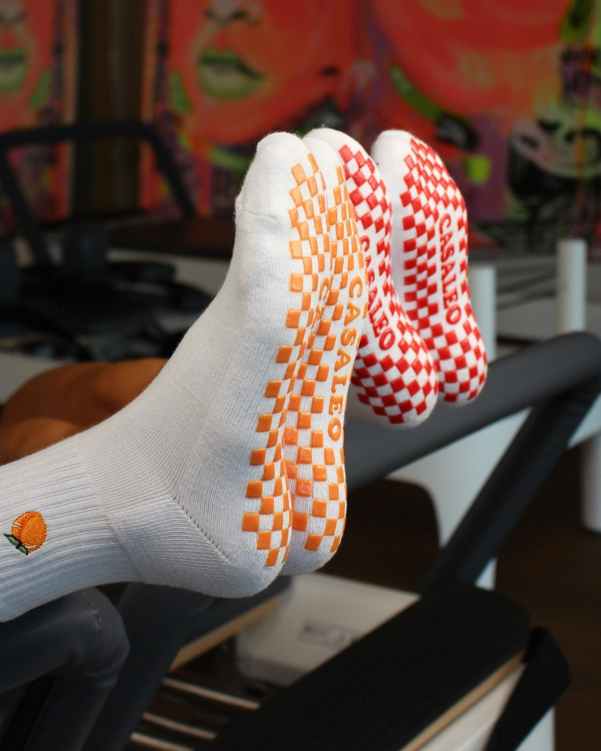 casaleo Grip Socken mit roter Grip Sohle und Kirsch Icon und orangener Grip Sohle und Pfirsich Icon auf dem Reformer Gerät